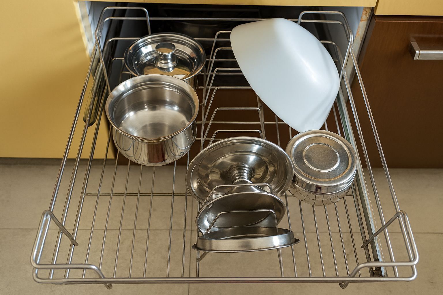 A kitchen with a metal drying rack holding various stainless steel pots and pans.