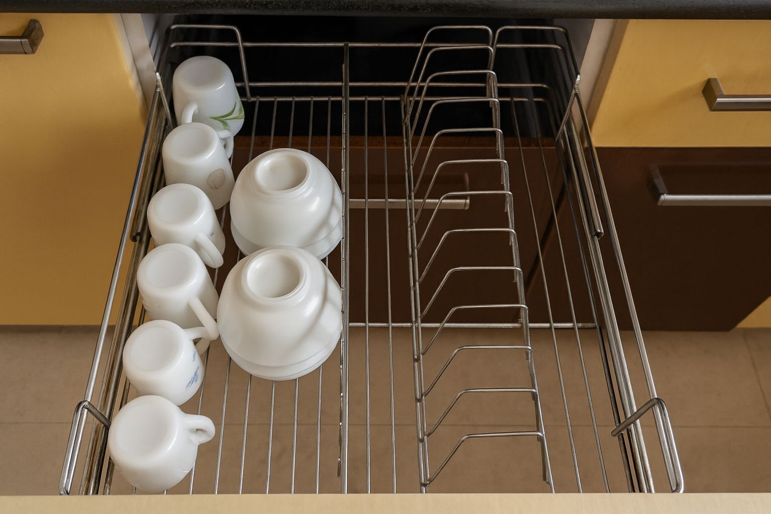 A kitchen with a metal rack holding white cups and a teapot.
