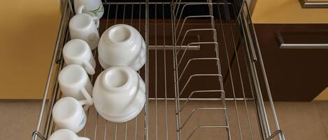 A kitchen with a metal rack holding white cups and a teapot.