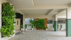A spacious indoor area with a tiled floor, a vertical garden on the left, and a wooden panel wall with plants in the center. - White Fern Stays (Hyderabad)