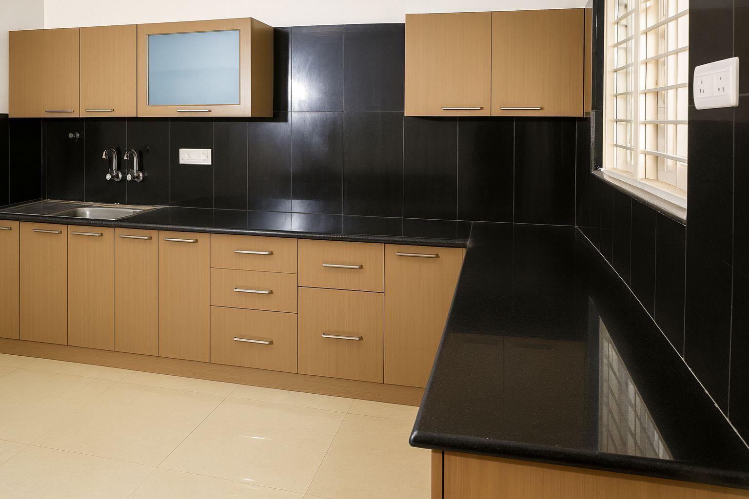 A modern kitchen with black countertops, wooden cabinets, and a window with blinds.