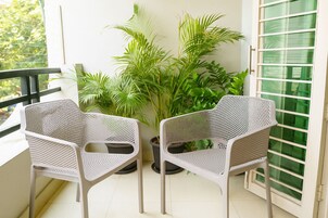 Two white wicker chairs on a balcony with potted plants and a green glass door.