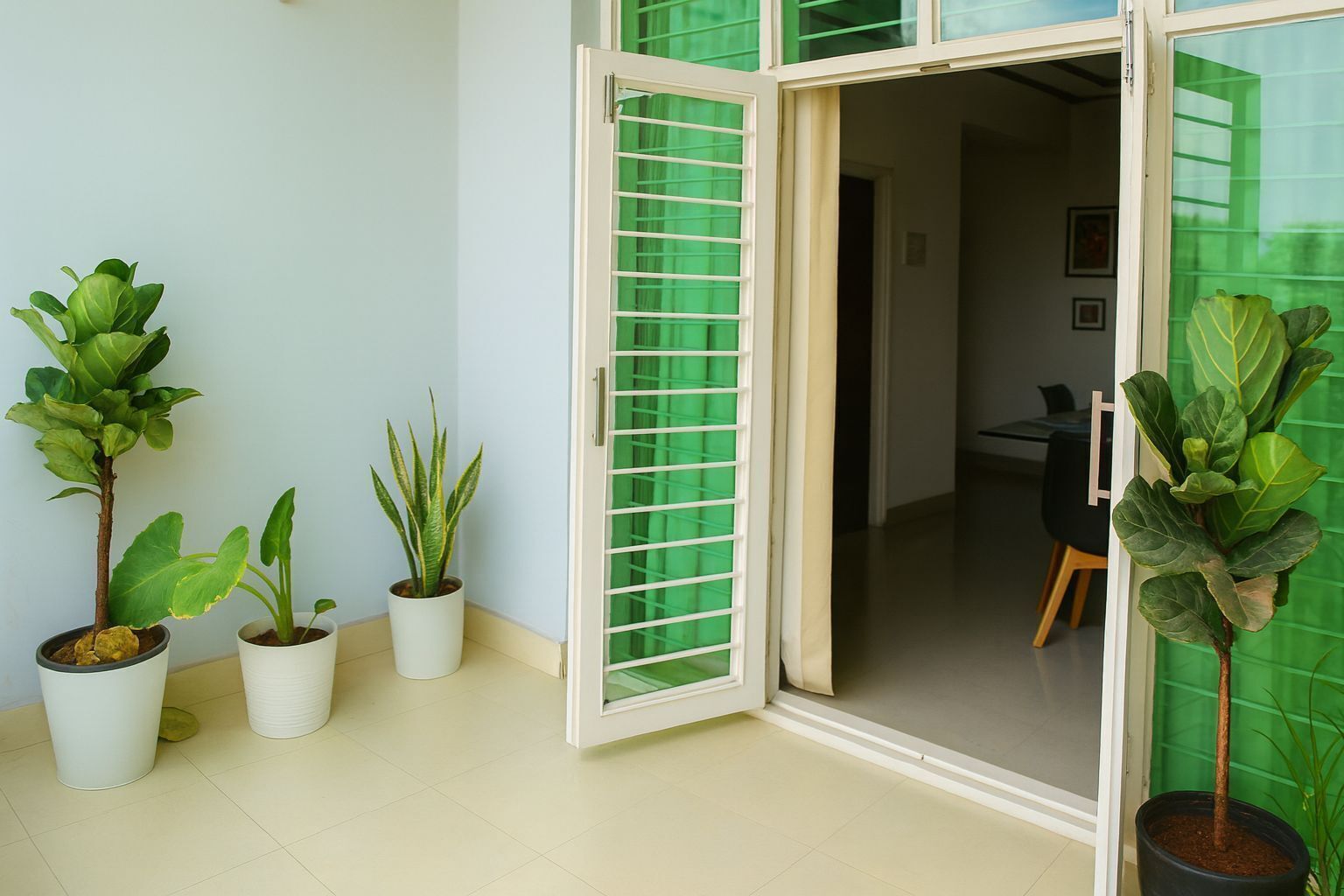 Habitación con puerta corrediza de vidrio que da a un balcón, plantas en macetas y vista hacia un comedor.