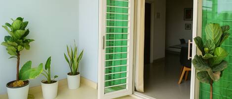 Habitación con puerta corrediza de vidrio que da a un balcón, plantas en macetas y vista hacia un comedor.