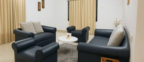 A modern living room with two dark sofas, a small white coffee table, and beige curtains.