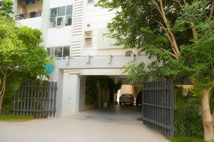 A modern two-story building with a gated entrance, a covered driveway, and lush greenery.