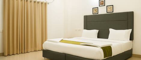 A modern hotel room with a large bed, a grey headboard, and beige curtains.