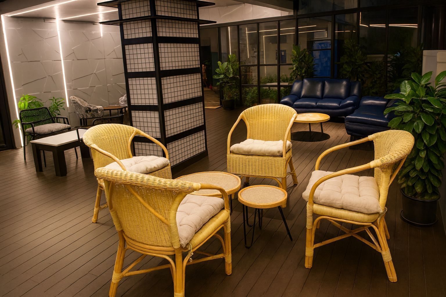 A modern lounge area with wicker furniture, a glass partition, and potted plants.