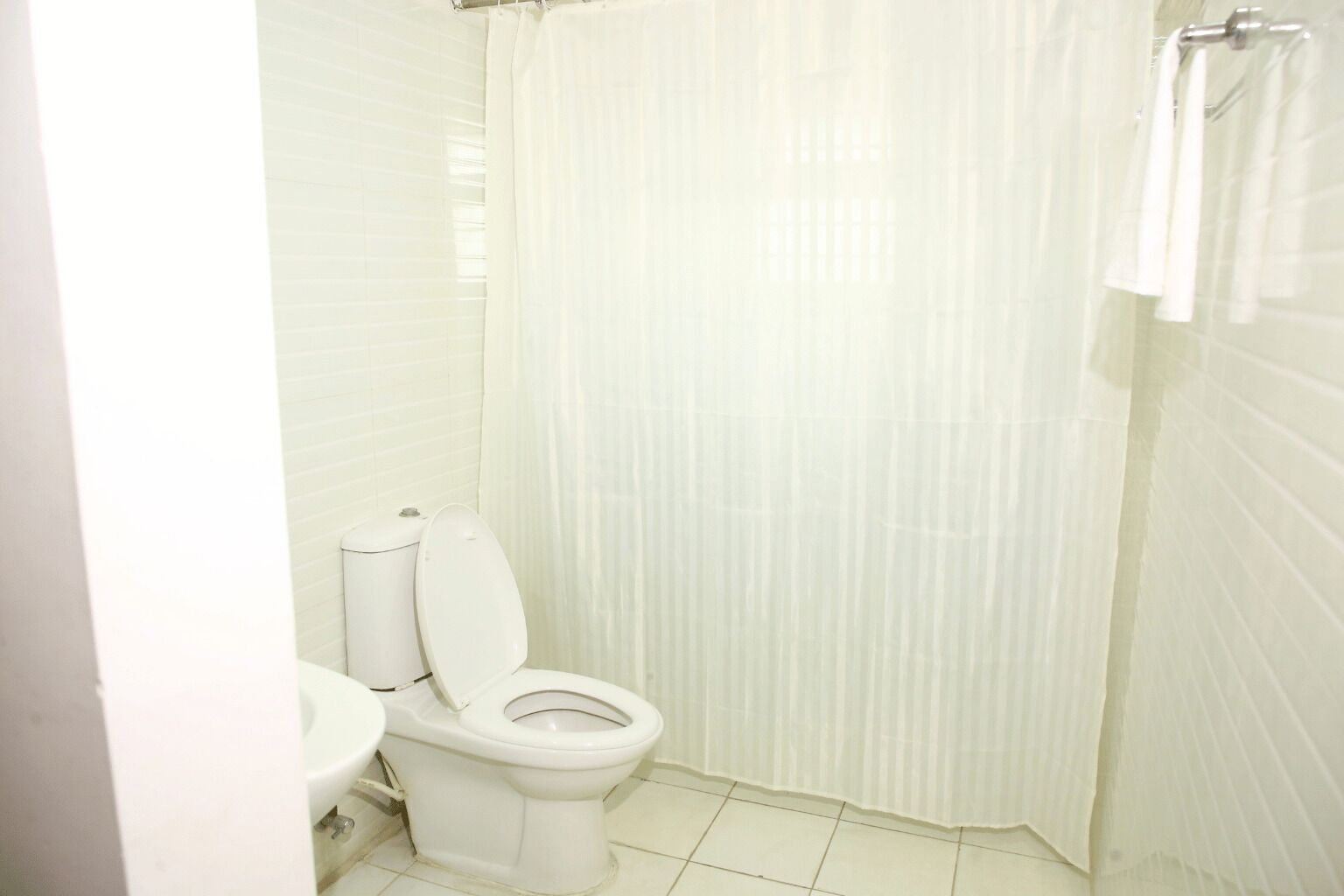 A small, white bathroom with a toilet, sink, and shower curtain.