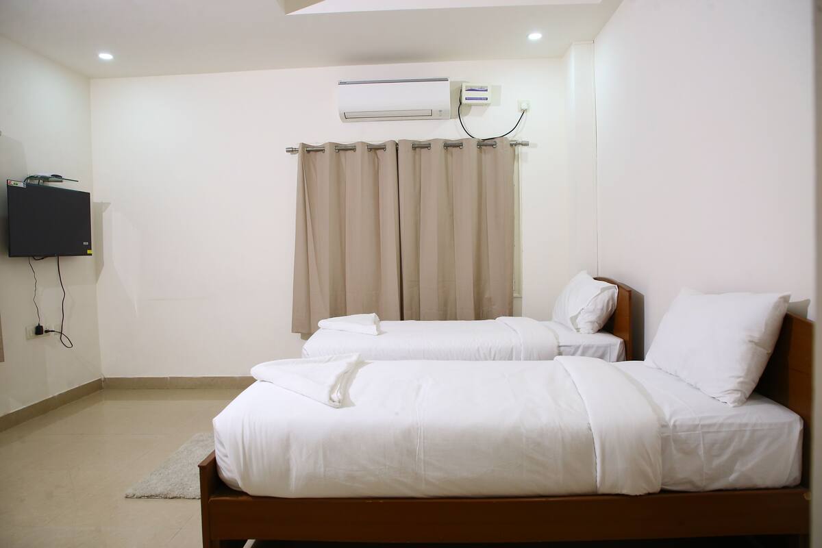 Ein Hotelzimmer mit zwei Betten, einem Flachbildfernseher, einer Klimaanlage und einem Vorhang.