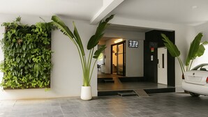 A modern hotel entrance with a green wall, a potted plant, a car parked outside, and a staircase leading to the interior. - White Fern Stays (Hyderabad)