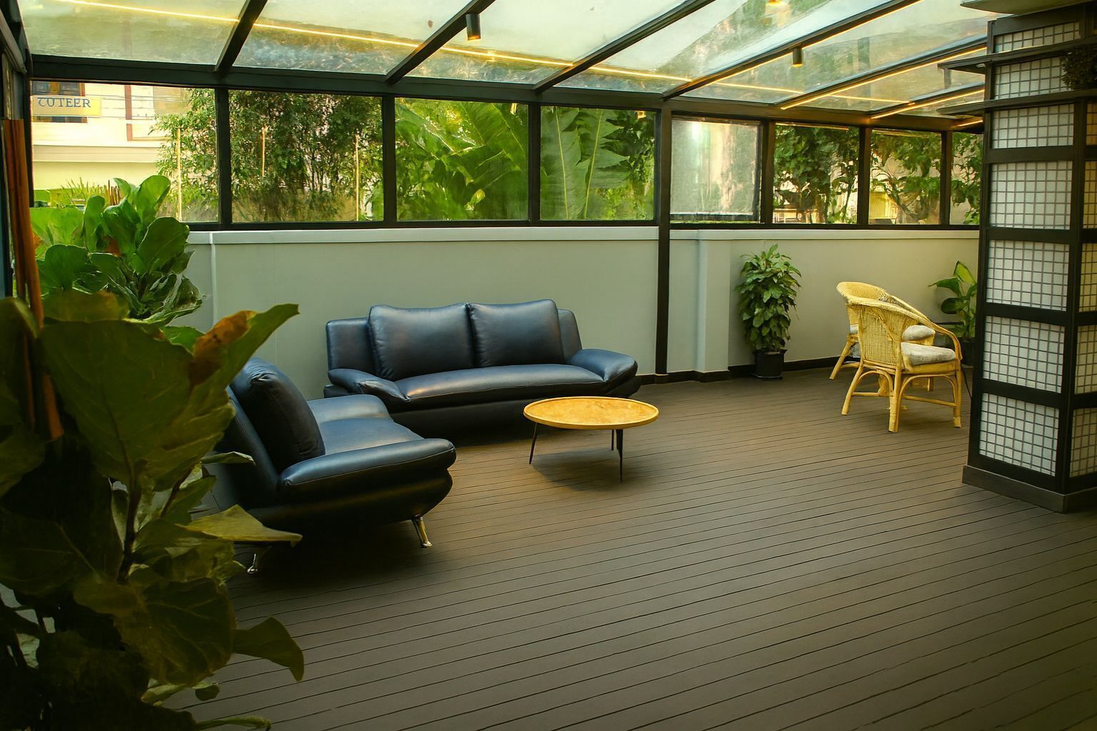 A conservatory with a wooden floor, a black leather sofa, a round yellow coffee table, and wicker chairs.