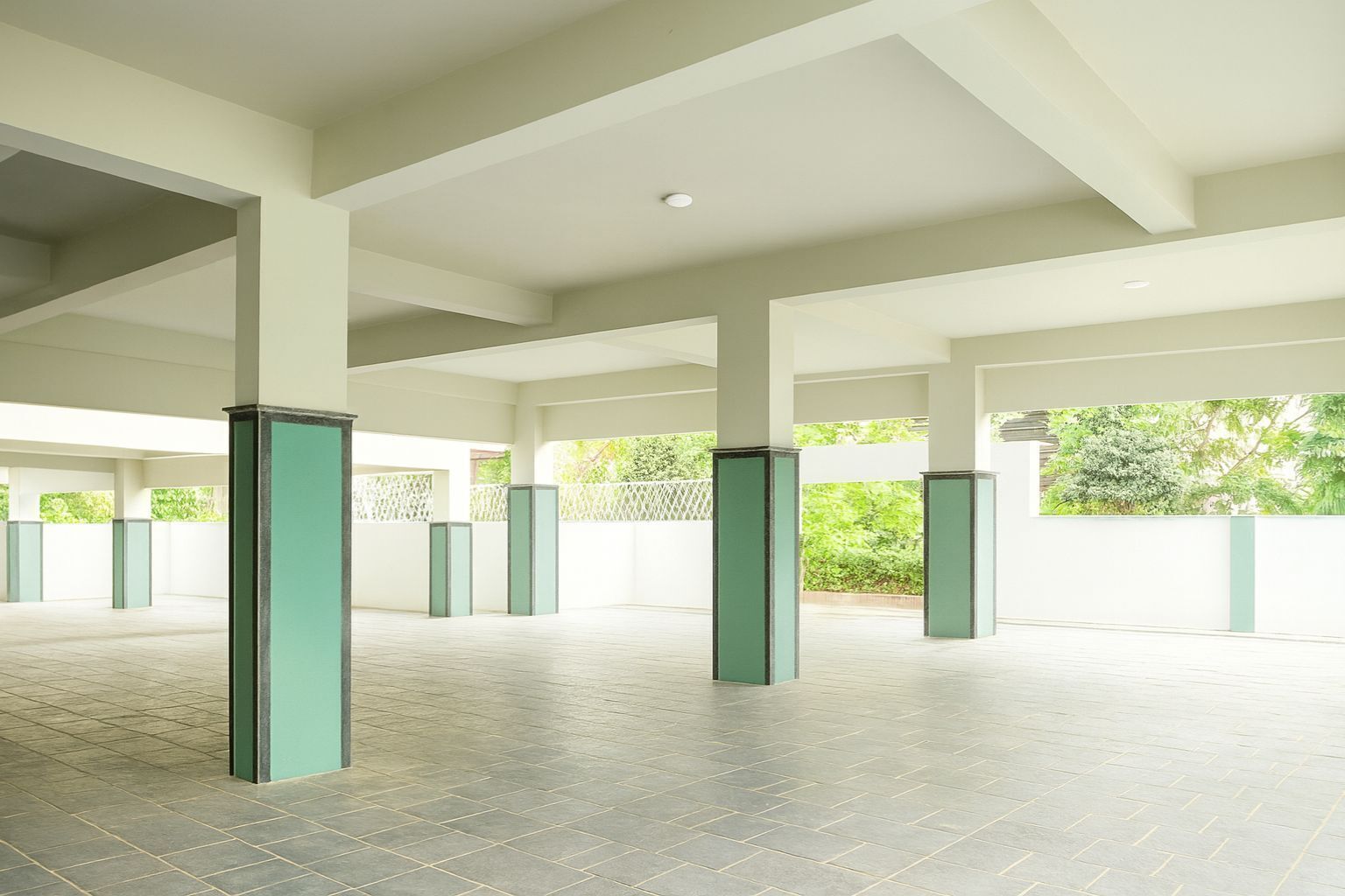 Um espaço interno com pé direito alto, paredes brancas e pilares verdes.