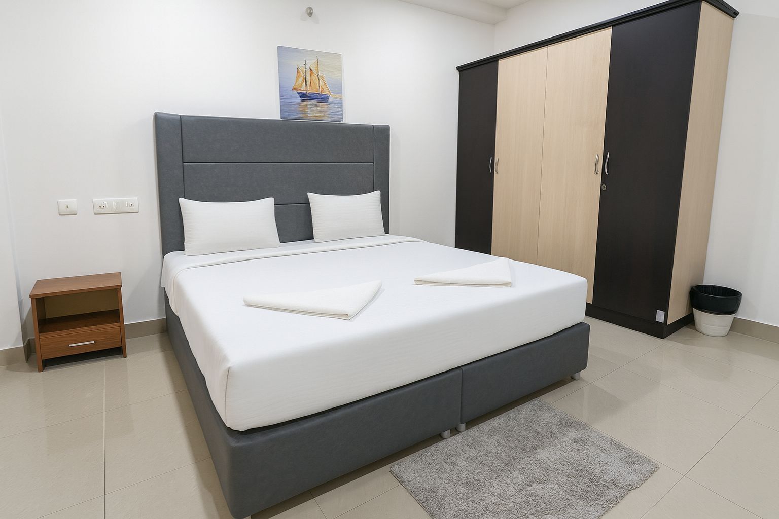 A bedroom with a bed, bedside table, wardrobe, and a painting on the wall.