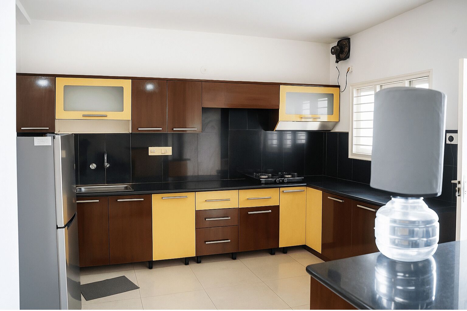 A kitchen with dark wooden cabinets, a black countertop, and a stainless steel refrigerator.