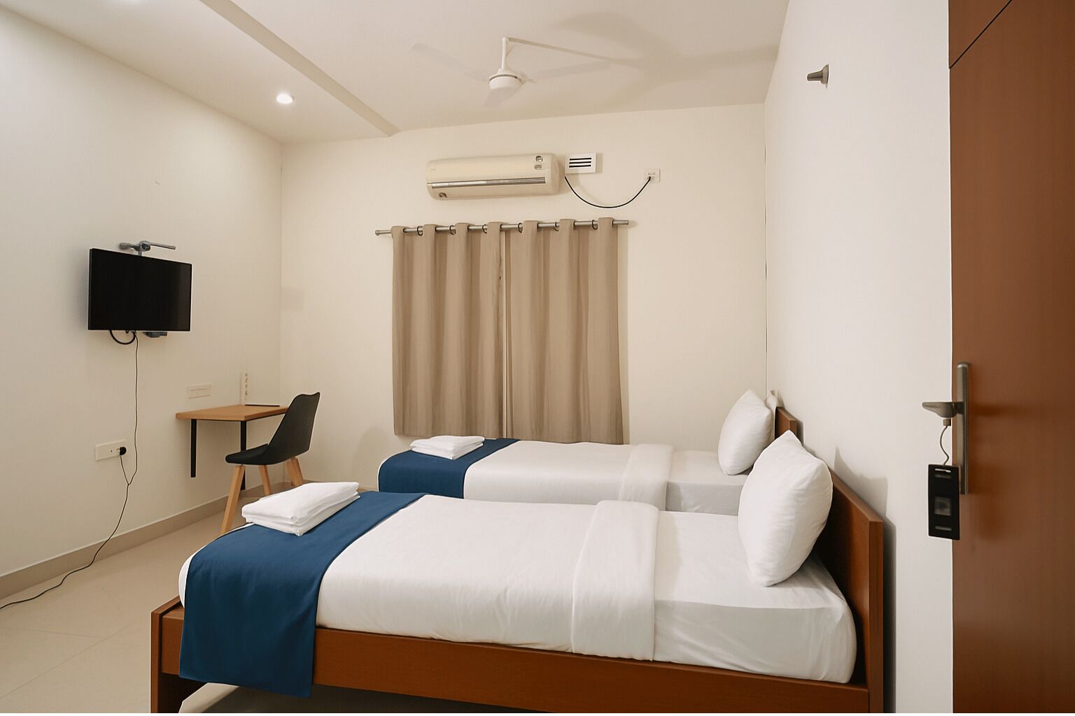 Een hotelkamer met twee bedden, een bureau, een stoel, een televisie en een airconditioning.