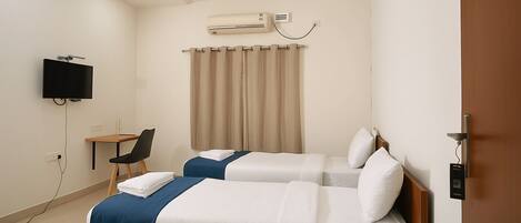 A hotel room with two beds, a desk, a chair, a television, and an air conditioning unit.