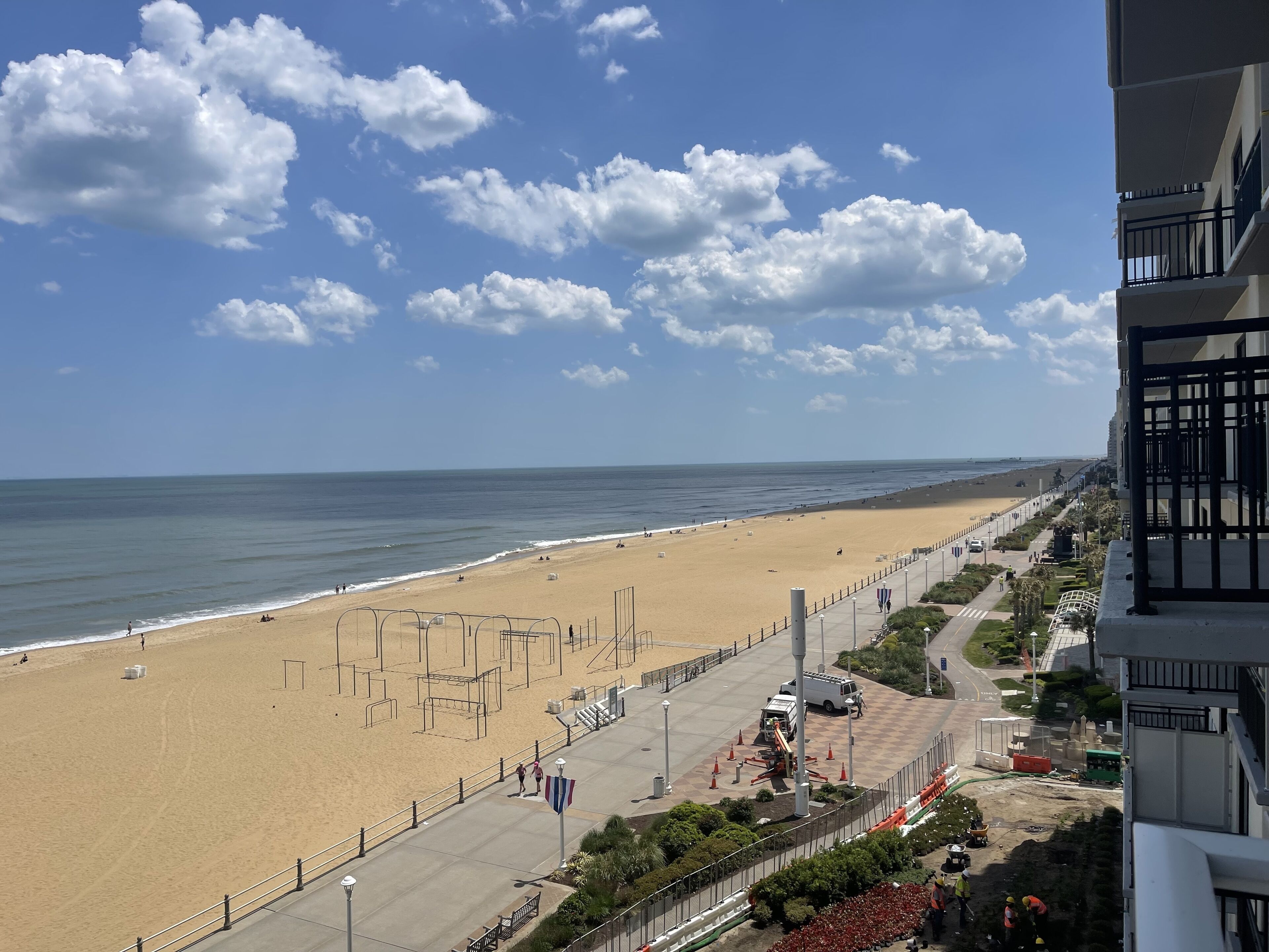 Een strand met heldere lucht, een zandstrand en een boulevard met gebouwen en begroeiing.