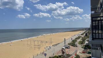Een strand met heldere lucht, een zandstrand en een boulevard met gebouwen en begroeiing.