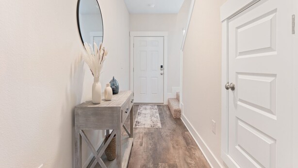 Un couloir avec une porte blanche, une console en bois agrémentée d’objets décoratifs et un tapis sur le sol.