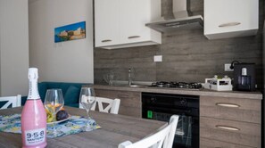 Una cocina moderna con estufa a gas, cafetera y lavaplatos. Hay una mesa de comedor con una botella de vino rosado y copas.
