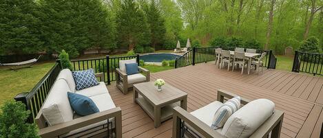 An outdoor deck with a pool, surrounded by lush greenery and furnished with sofas and a dining set.