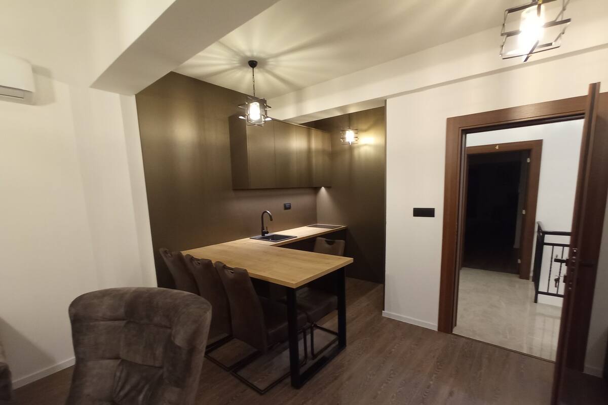 Eine kleine Küche mit Holztisch und Stühlen, einem eingebauten Backofen und Pendelleuchten.