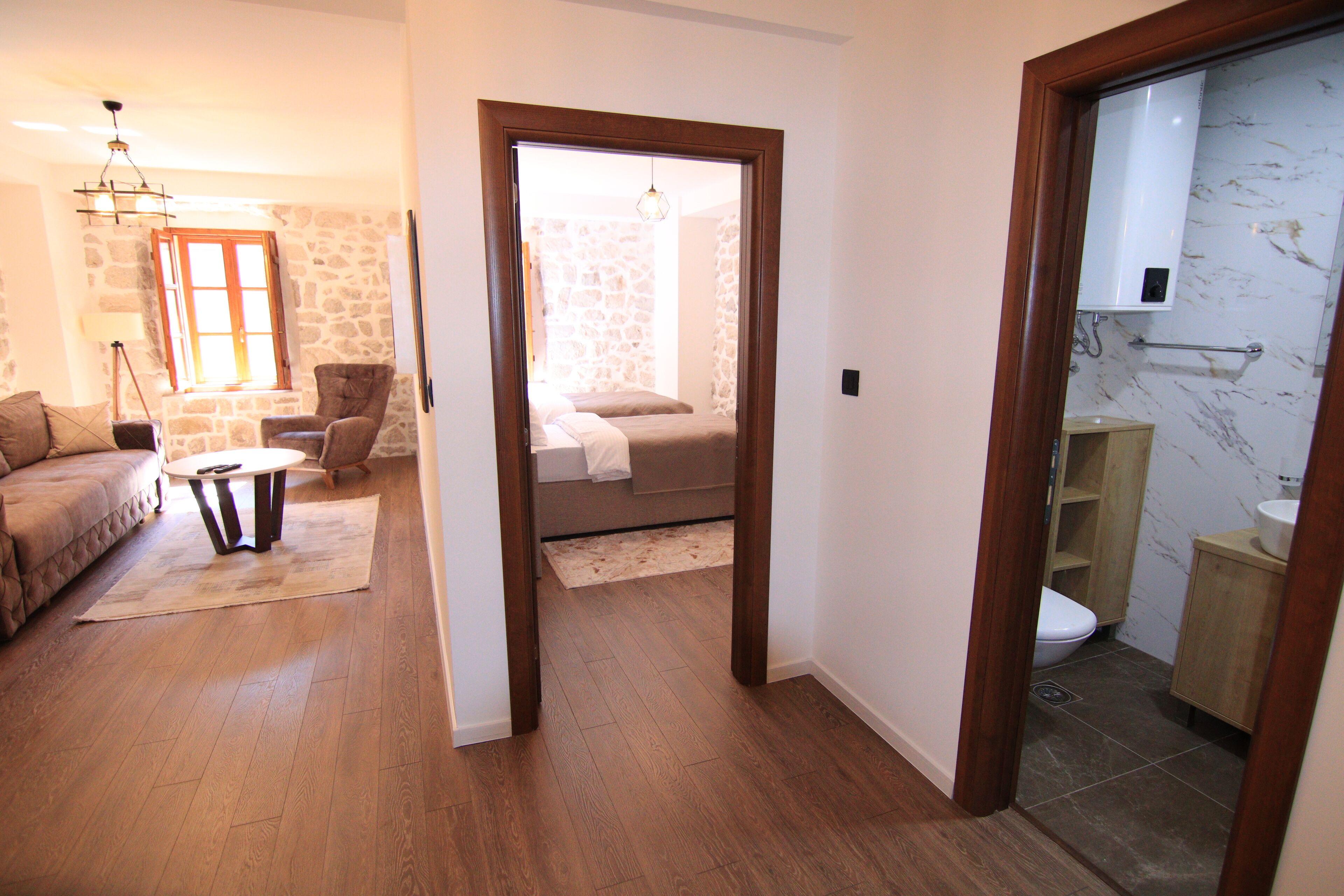 A spacious living room with a sofa, a coffee table, and a stone wall. A bathroom with a toilet, sink, and marble backsplash is visible through an open door.