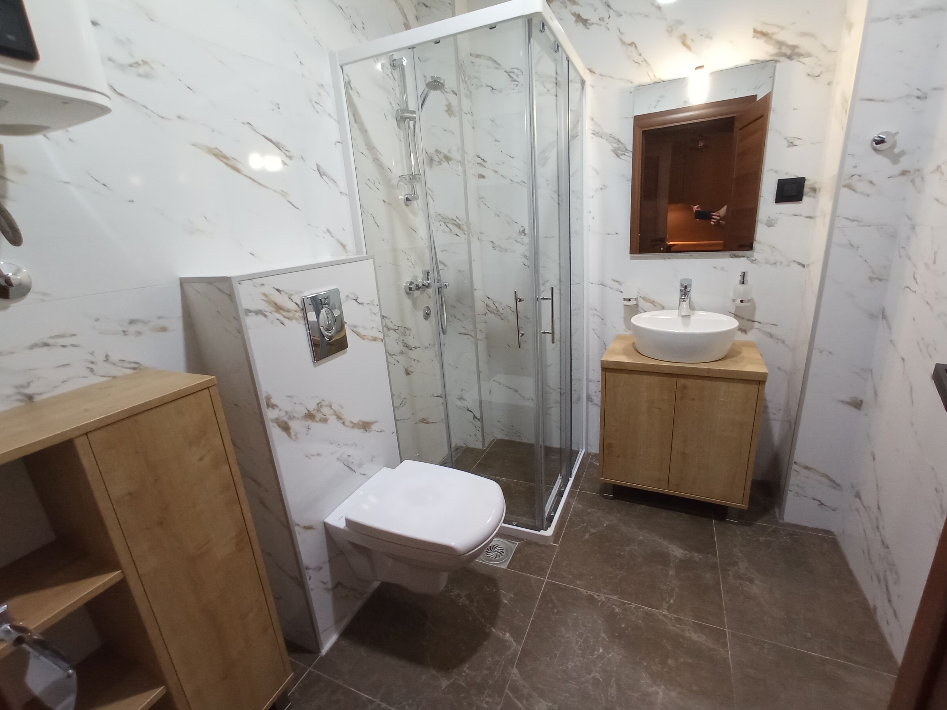 A bathroom with a toilet, a sink, a shower enclosure, and a wooden cabinet.