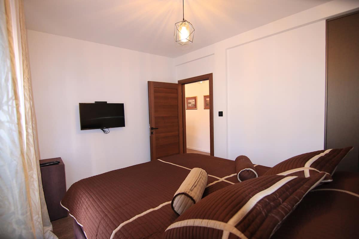 Ein Schlafzimmer mit einem Bett, einem an der Wand montierten Fernseher, einer Tür und einer Leuchte.