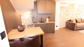 A compact kitchen with a wooden table and chairs, a stone wall, and a sofa in the adjacent living area.