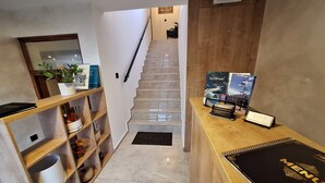 A hotel reception area with a wooden desk, a black menu stand, and a staircase leading to the upper floor.