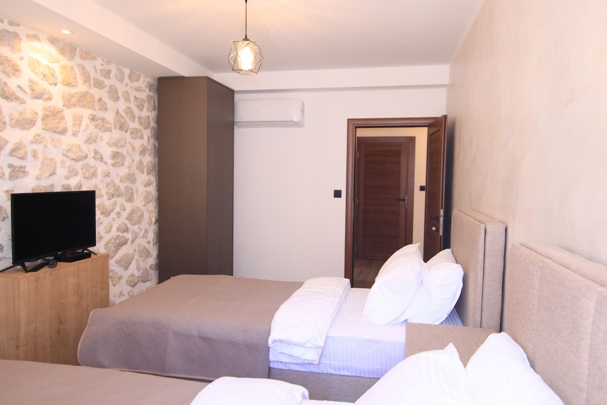 Ein Hotelzimmer mit Steinwand, Flachbildfernseher, zwei Betten mit weißer Bettwäsche und einer Holztür.