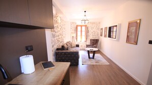 A modern kitchen with a wooden countertop, a sink, and a stone wall. There is a dining area with a table and chairs, and a sofa in the background.