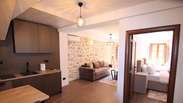 A modern kitchen with wooden cabinets, a dining table, and a stone wall. There is a cozy living area with a sofa and a small table.
