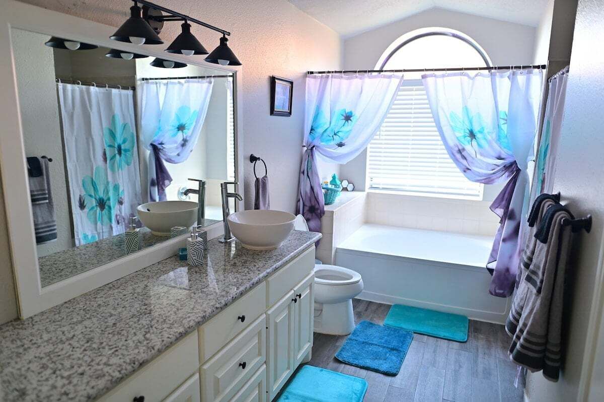 Un bagno con doppio lavandino, water, vasca e una finestra con tende.