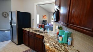 A kitchen with dark wooden cabinets, a granite countertop, a stainless steel refrigerator, and a microwave. - Heated 3BR • Furnished • WiFi • Laundry • Fort Sam w/ Wi-Fi & W/D (San Antonio)