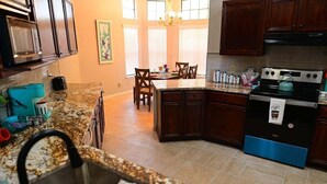 A kitchen with granite countertops, dark wooden cabinets, a stainless steel sink, a stove, and a dining area with chairs and a table. - Heated 3BR • Furnished • WiFi • Laundry • Fort Sam w/ Wi-Fi & W/D (San Antonio)