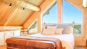 A bedroom with a wooden ceiling, a large bed, and a view of the landscape. - Hill Cabin Hideaway, Romantic! Country Cabin for 2 (North Powder)