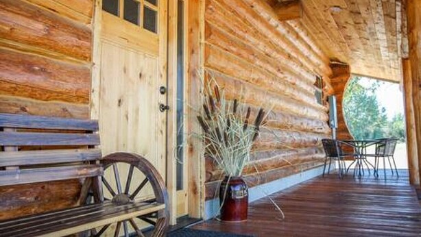 A log cabin with a wooden porch, a wooden door, and a table with chairs. - Hill Cabin Hideaway, Romantic! Country Cabin for 2 (North Powder)