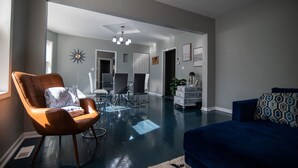 Ein modernes Wohnzimmer mit einem blauen Sofa, einem orangefarbenen Sessel und einem Essbereich mit Stühlen und einem Tisch.