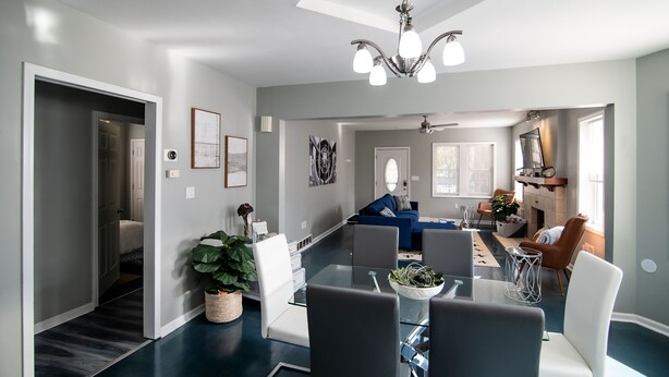 Ein modernes Wohnzimmer mit einem Glastisch, weißen und grauen Stühlen, einem blauen Sofa und einem Kamin.