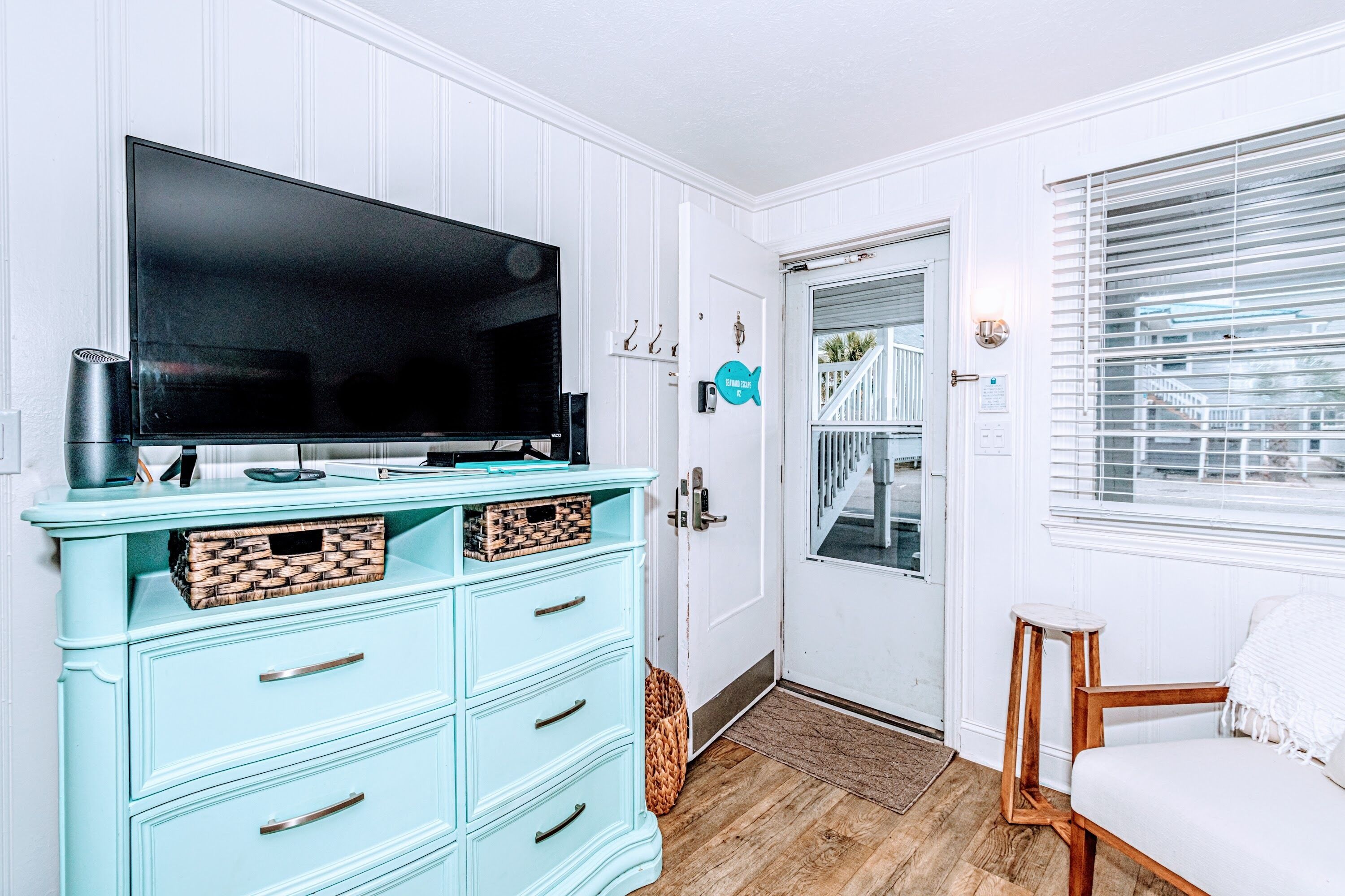 A room with a teal dresser, a flat-screen TV, and a wooden chair.