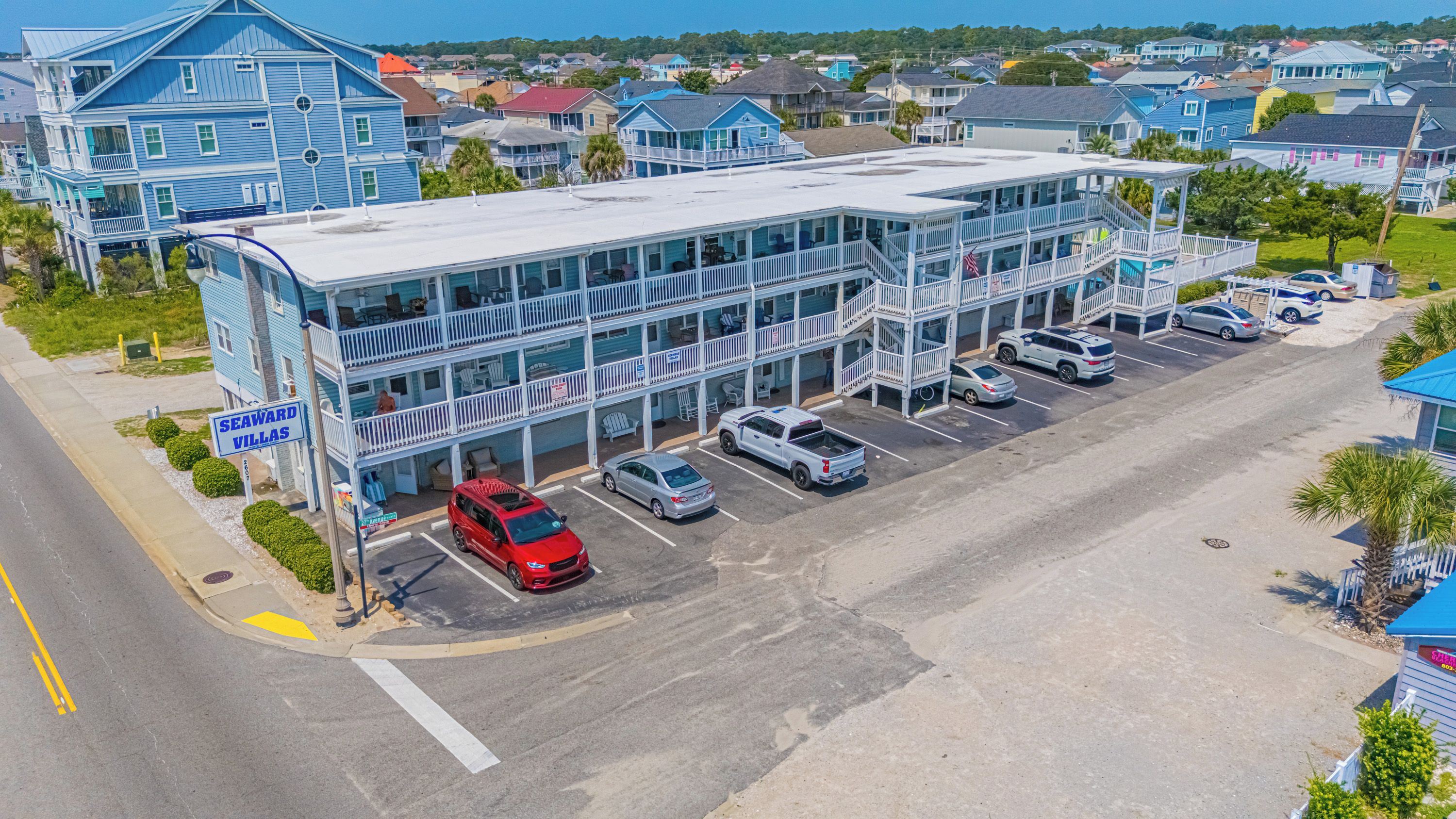 Un hôtel à plusieurs étages avec un parking, une voiture rouge garée devant et une enseigne indiquant « Seaward Villas ».
