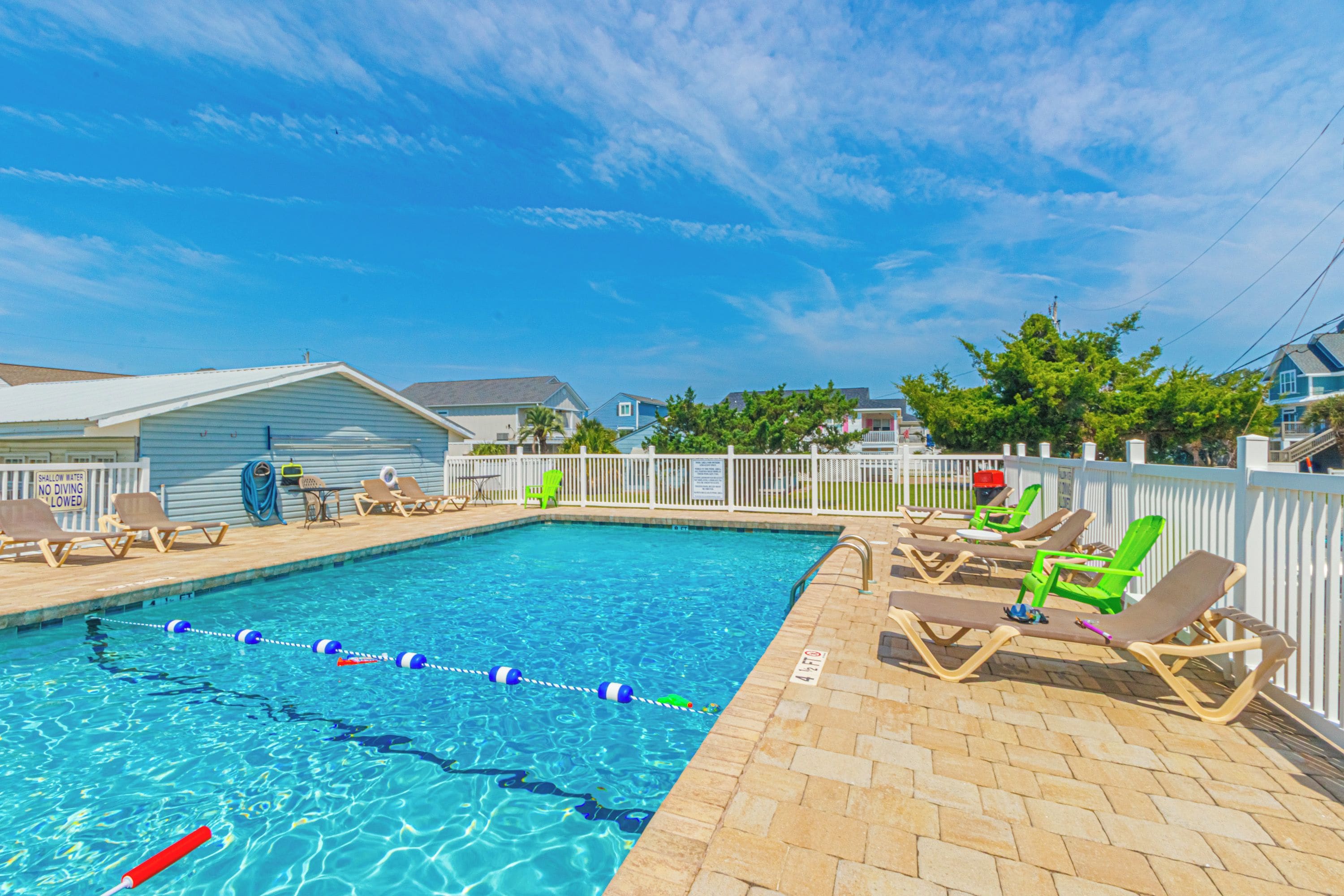 A swimming pool with lounge chairs and a fence, surrounded by houses.