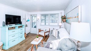 Una sala de estar con televisor, sofá, sillón, lámpara y un cuadro en la pared.