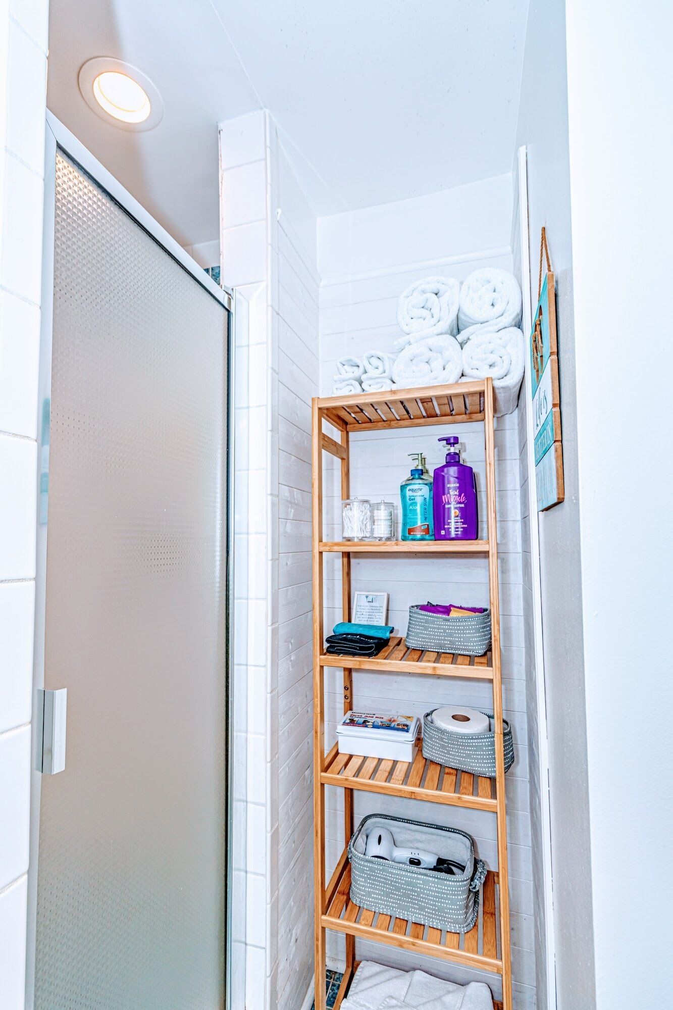 Une salle de bain avec une étagère en bois où sont rangés les articles de toilette, les serviettes et un tableau encadré.