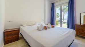 Une chambre d’hôtel avec un lit, une table de chevet en bois, une commode et une fenêtre avec des rideaux.