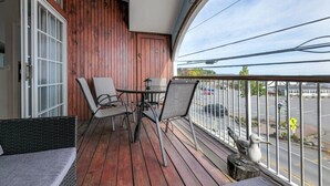 Uma varanda de madeira com mesa e cadeiras, vista para a rua, e uma estátua de pássaro.