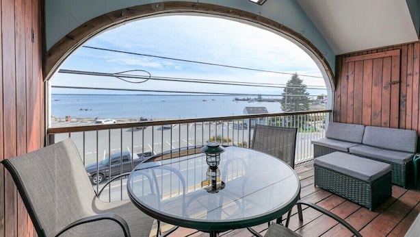 Een balkon met een glazen tafel en stoelen, een rieten bank en uitzicht op zee.